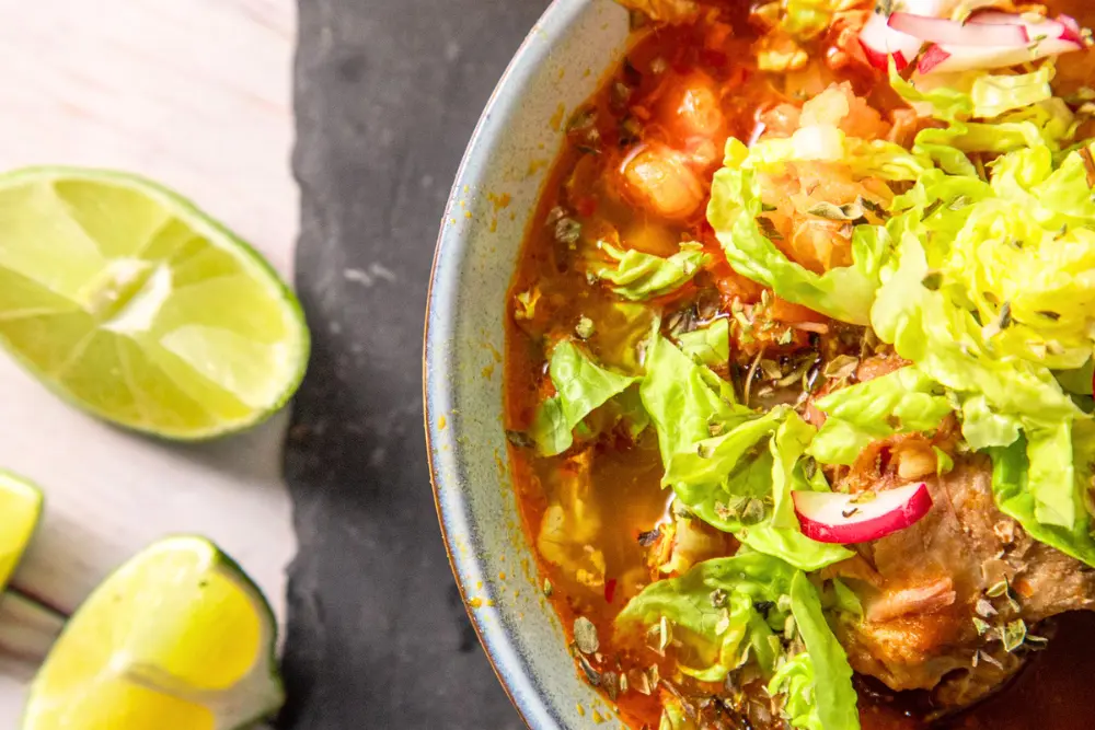 Traditional Mexican pozole with lettuce, radishes and lime
